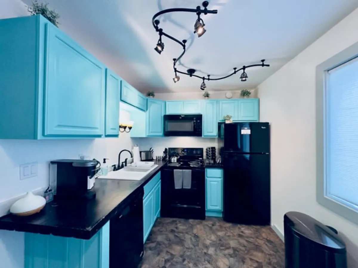This image features a vibrant kitchen with turquoise cabinets, modern black appliances, and striking countertops. The cheerful décor invites guests to prepare meals, entertain, and gather—echoing the feeling of home and the hospitality aspect.