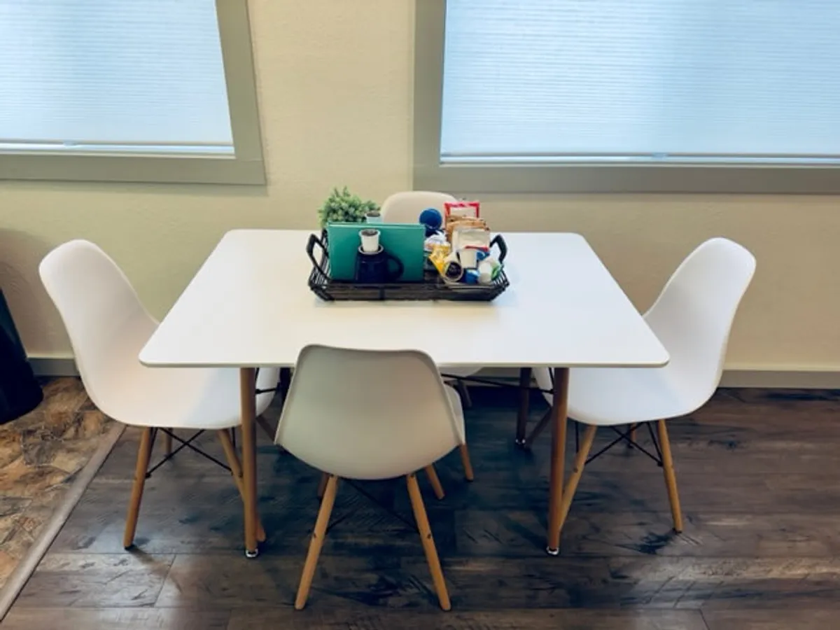 A cozy dining nook with a white dining table surrounded by comfortable chairs, set up for a casual meal or coffee break. The simple tray with items on the table evokes a setting ideal for family dinners, celebratory meals, or relaxed bites after a day outdoors.