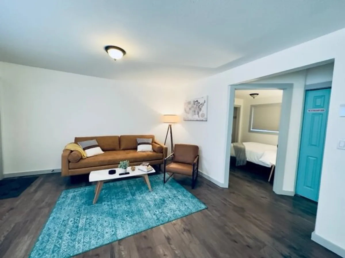This image displays a cozy living room with a comfortable sofa, a coffee table, a soft area rug, a lamp, and tasteful artwork. The space appears inviting and ideal for relaxation, reading, or enjoying a quiet coffee, embodying the atmosphere of a welcoming home base.