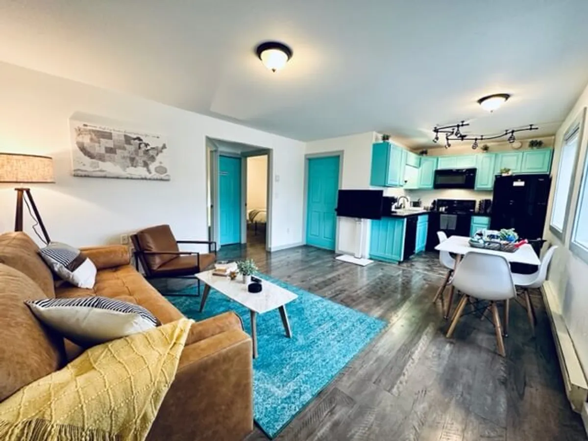 A modern living space with a comfortable sofa, dining table, kitchen area, and a decorative rug. The arrangement invites both relaxing and socializing, with ample natural light streaming in. This area supports group activities such as game nights or shared meals, matching the section's focus on togetherness and comfort.