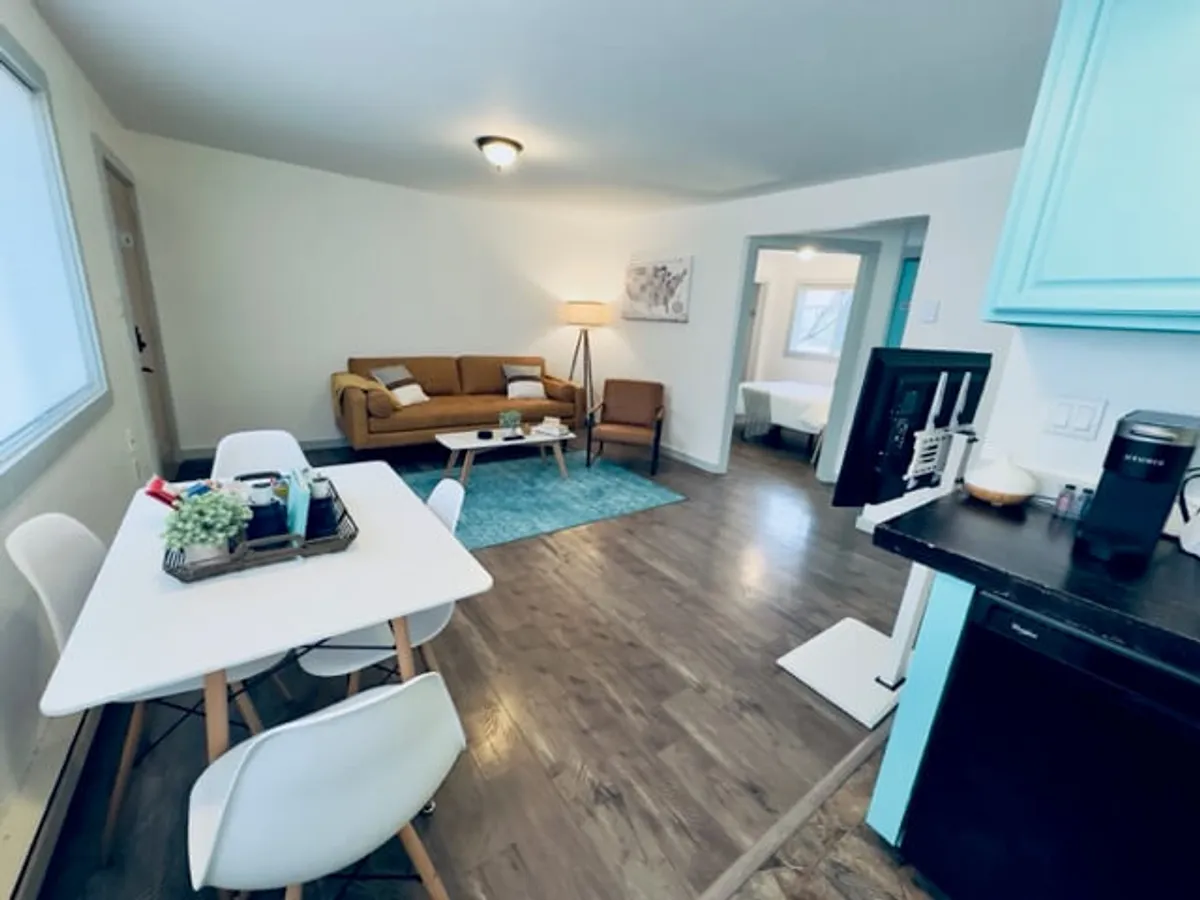 A spacious living area featuring a comfortable sofa, a stylish dining table, a patterned rug, and a lamp. The sofa invites relaxation, while the dining table is perfect for shared meals or board games. The open layout connects seamlessly to the kitchen area, and natural light fills the space, creating a welcoming, homey atmosphere.