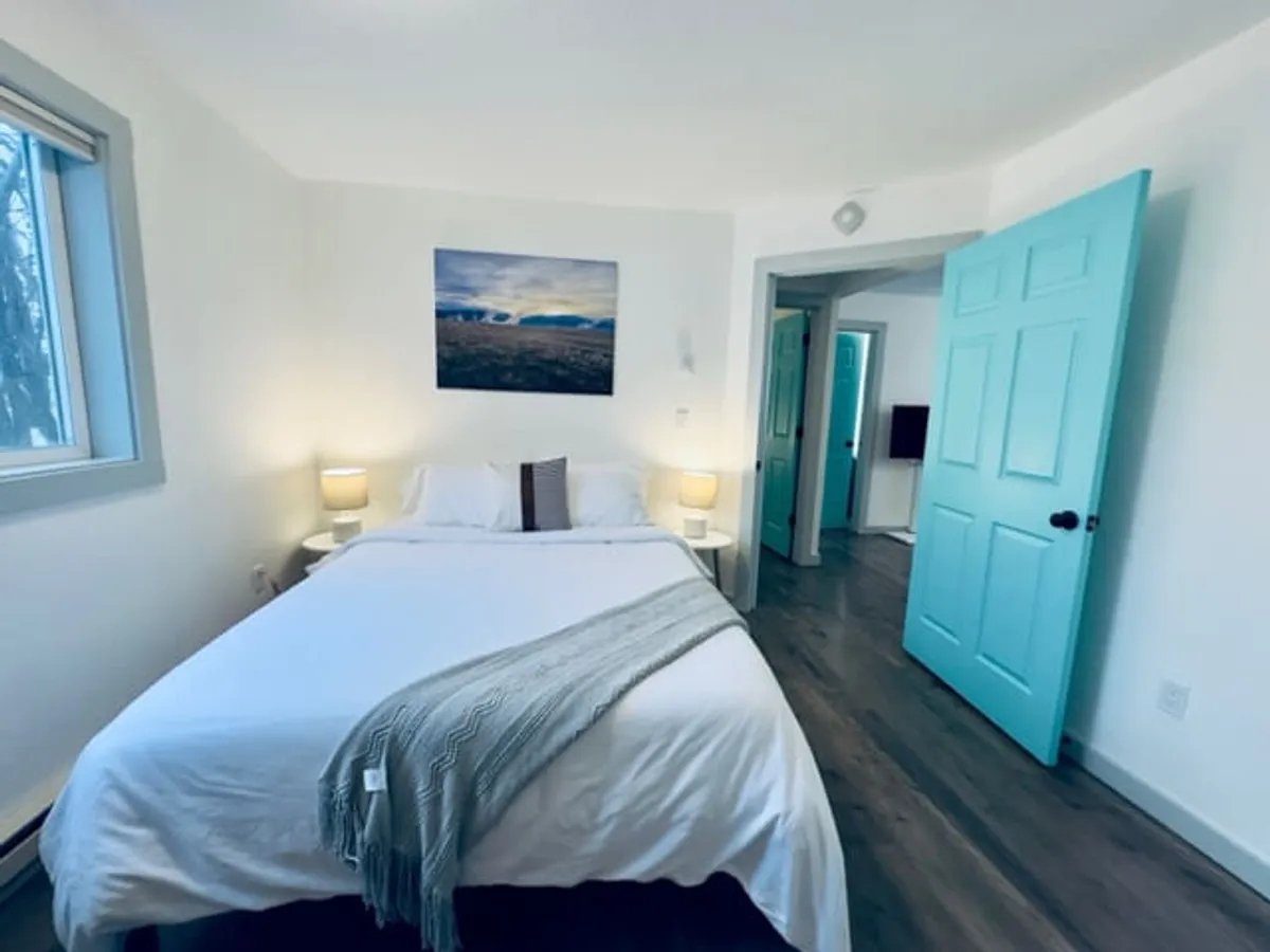 A serene bedroom featuring a plush bed dressed in soft linens, flanked by elegant blue doors and illuminated by gentle lamps. Wall art adds a personal, soothing touch, and the overall color palette is tranquil and calming. The space radiates an inviting atmosphere, ideal for rest and relaxation.