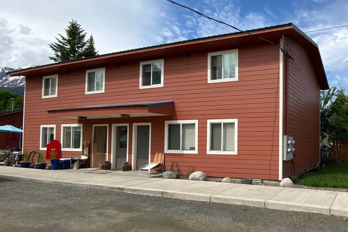 The property’s red exterior and welcoming front entrance are featured prominently, with outdoor seating available for relaxing on the porch. The image suggests a comfortable base from which to set out on adventures or unwind after a day exploring.