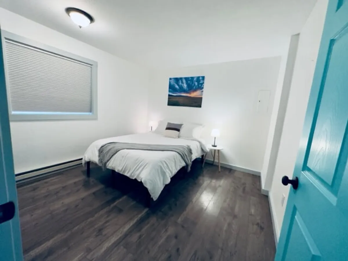 A tranquil bedroom with a comfortable bed adorned with cozy linens, accompanied by understated nightstands and soft wall art. Natural light filters in, enhancing the serene mood and making the space perfect for unwinding after a full day. The neutral tones and uncluttered design evoke a soothing retreat.
